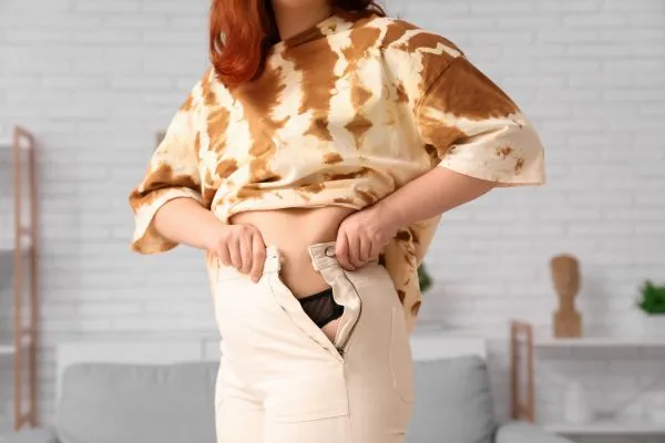 Image of woman trying to do her trousers up after pregnancy weight gain Shefford